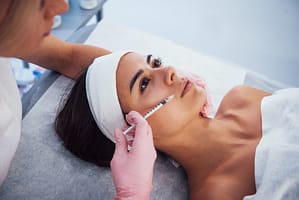 Woman lying down in spa and have injection by the syringe into her face skin