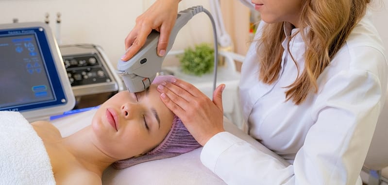 Cosmetologist making a woman a therapeutic laser processing on a face.
